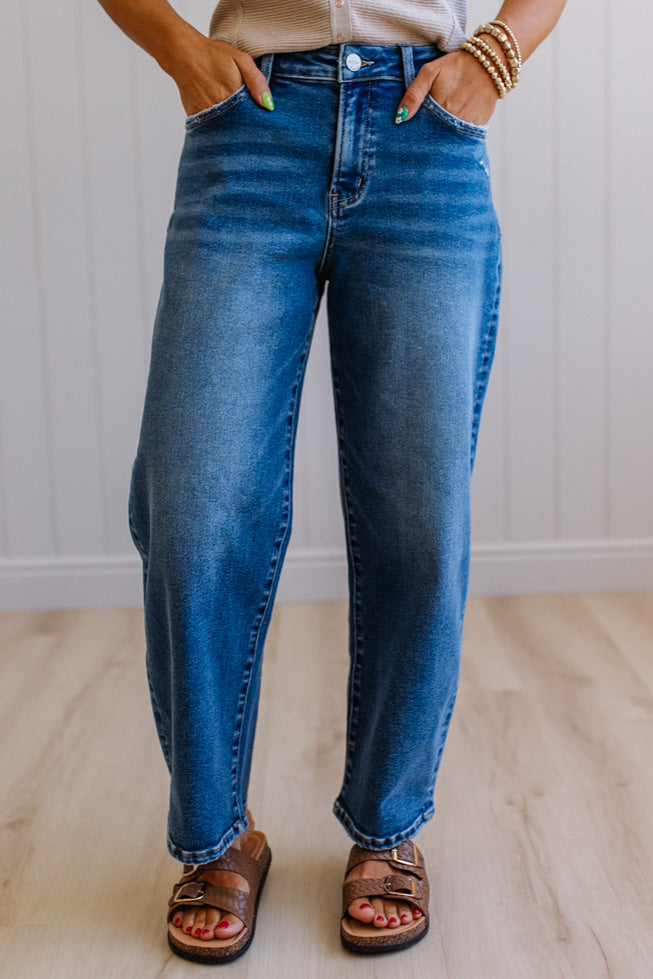 Person wearing blue jeans standing with hands in pockets against a neutral background
