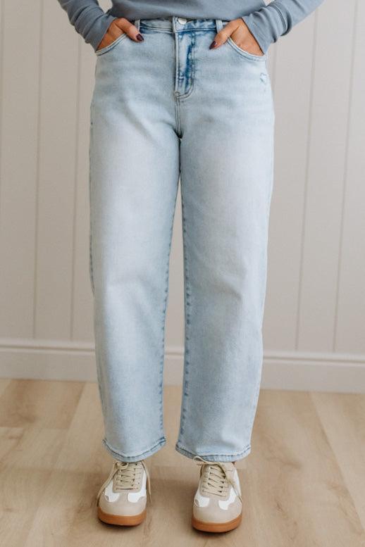 Person wearing light blue jeans and white sneakers against a neutral background