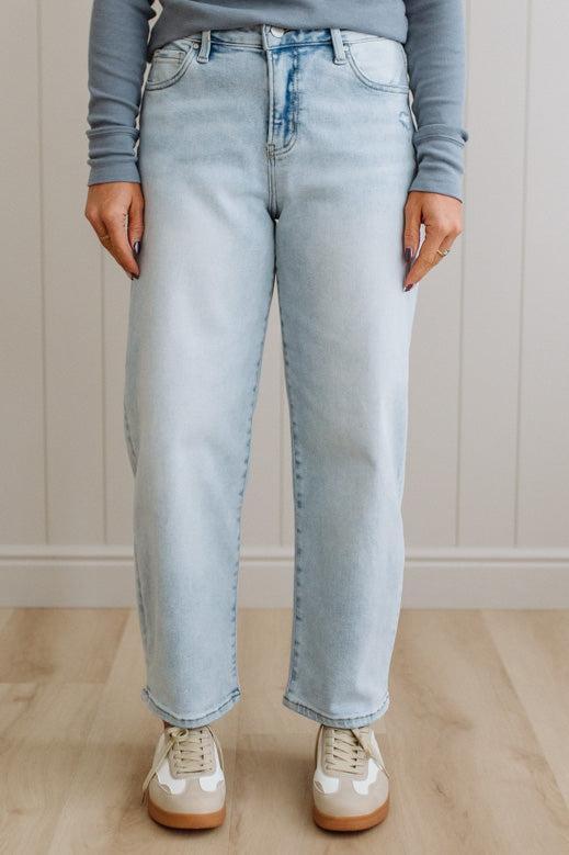 Person wearing light blue jeans and white sneakers on a wooden floor.