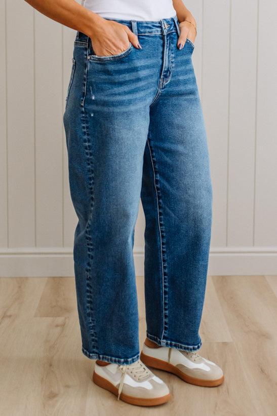 Person wearing blue jeans and white shoes on a wooden floor.