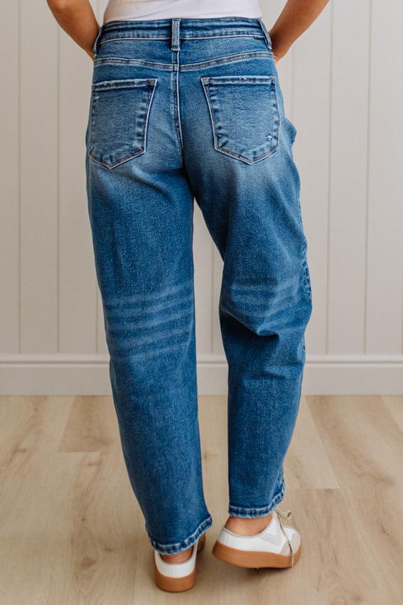 Person wearing blue jeans standing on a wooden floor with a white wall background