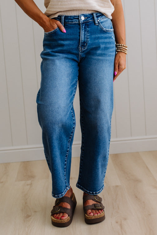 Person wearing blue jeans and sandals standing against a white paneled wall.