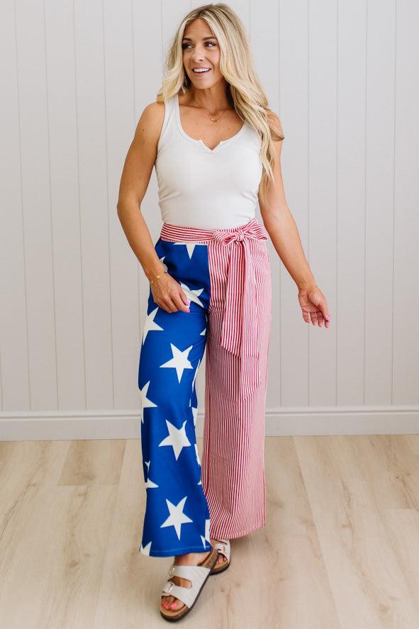 Woman wearing a white tank top and colorful pants with a red and white striped sash.