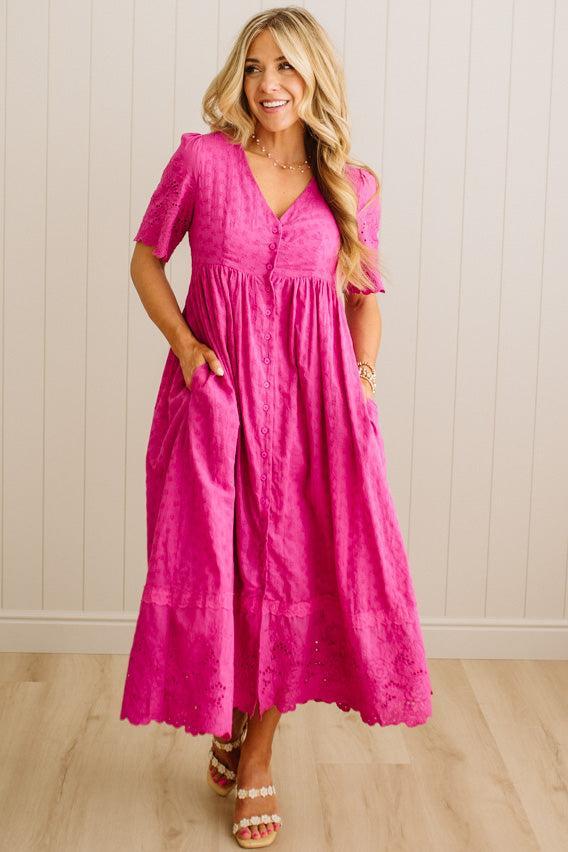 Woman wearing a pink dress standing against a white paneled wall.