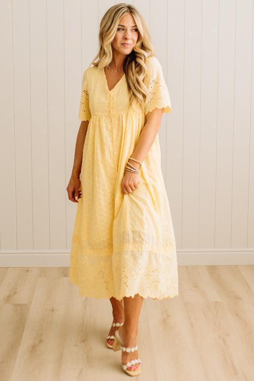 Woman wearing a yellow dress with lace details in a minimalistic setting.