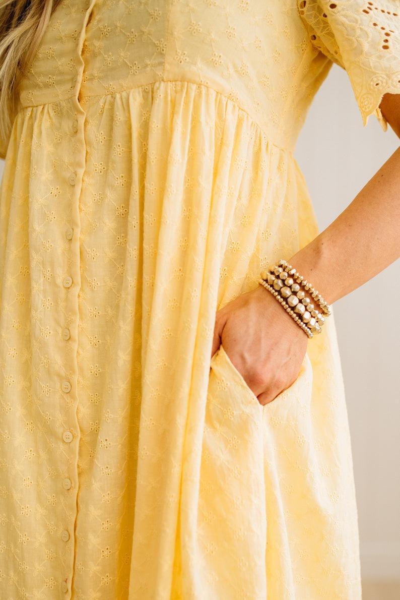 Yellow dress with a close-up of the fabric and a hand wearing a bracelet.