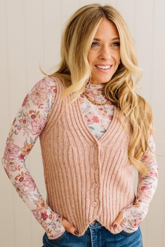 Woman wearing a pink vest over a floral long-sleeve shirt with a neutral background