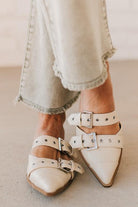 Woman in light green pants wearing cream chunky buckled slip-on flats.
