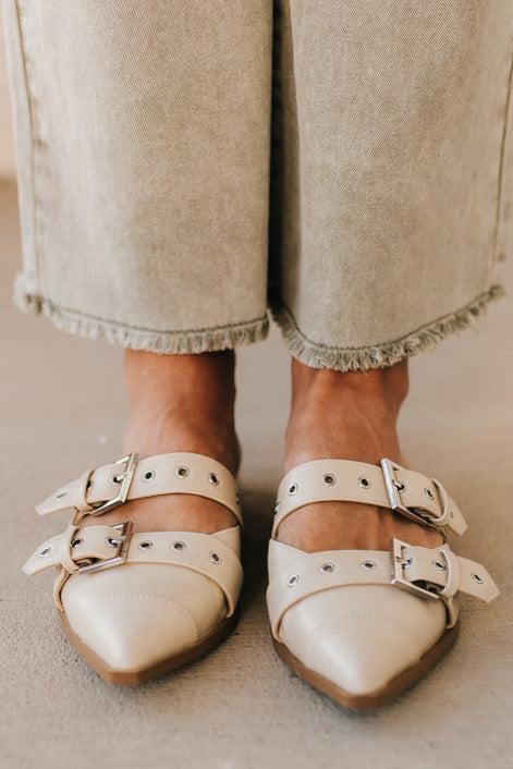 Woman in light green pants wearing cream chunky buckled slip-on flats.