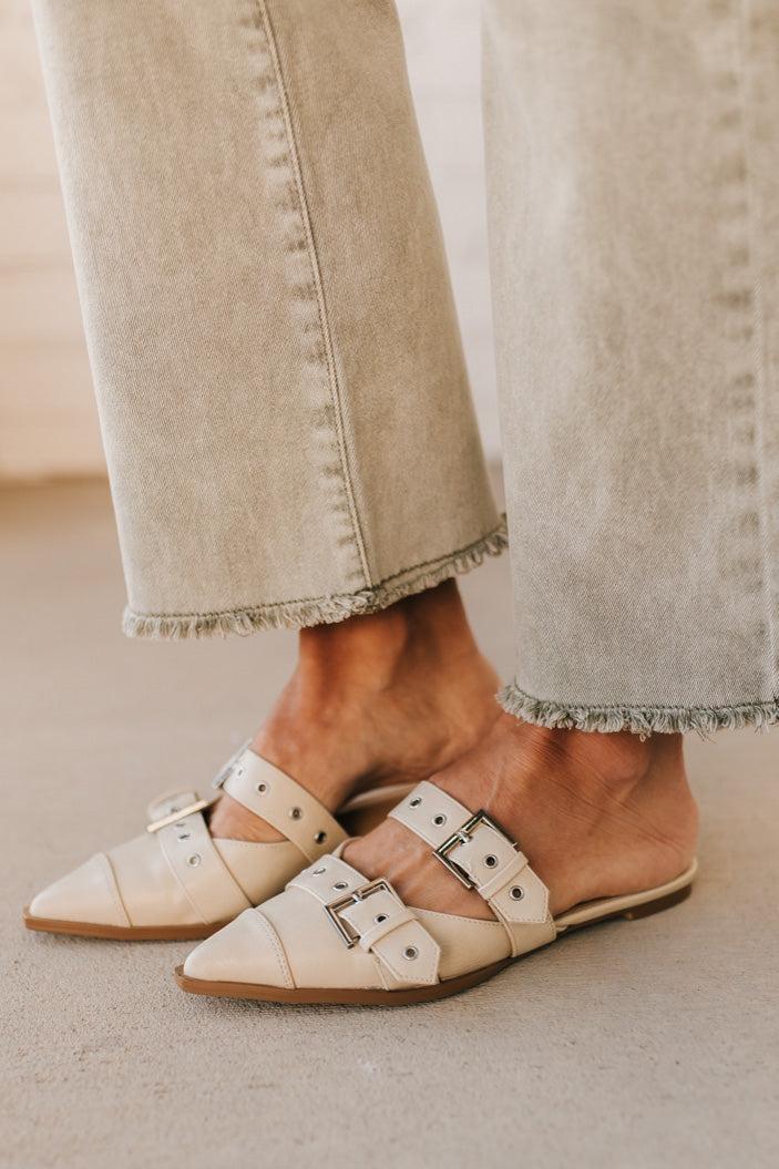 Woman in light green pants wearing cream chunky buckled slip-on flats.