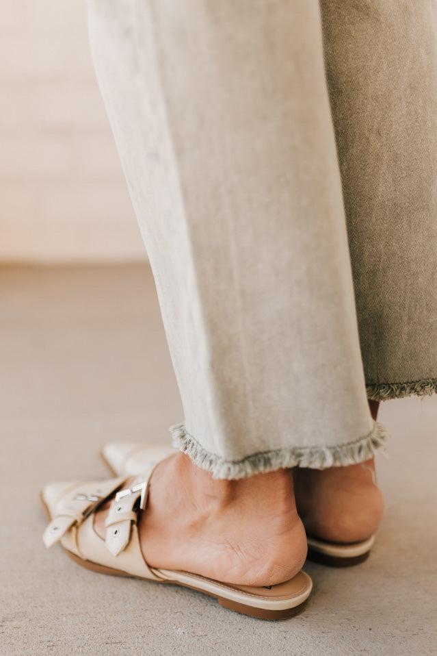Woman in light green pants wearing cream chunky buckled slip-on flats.