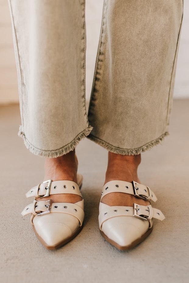 Woman in light green pants wearing cream chunky buckled slip-on flats.