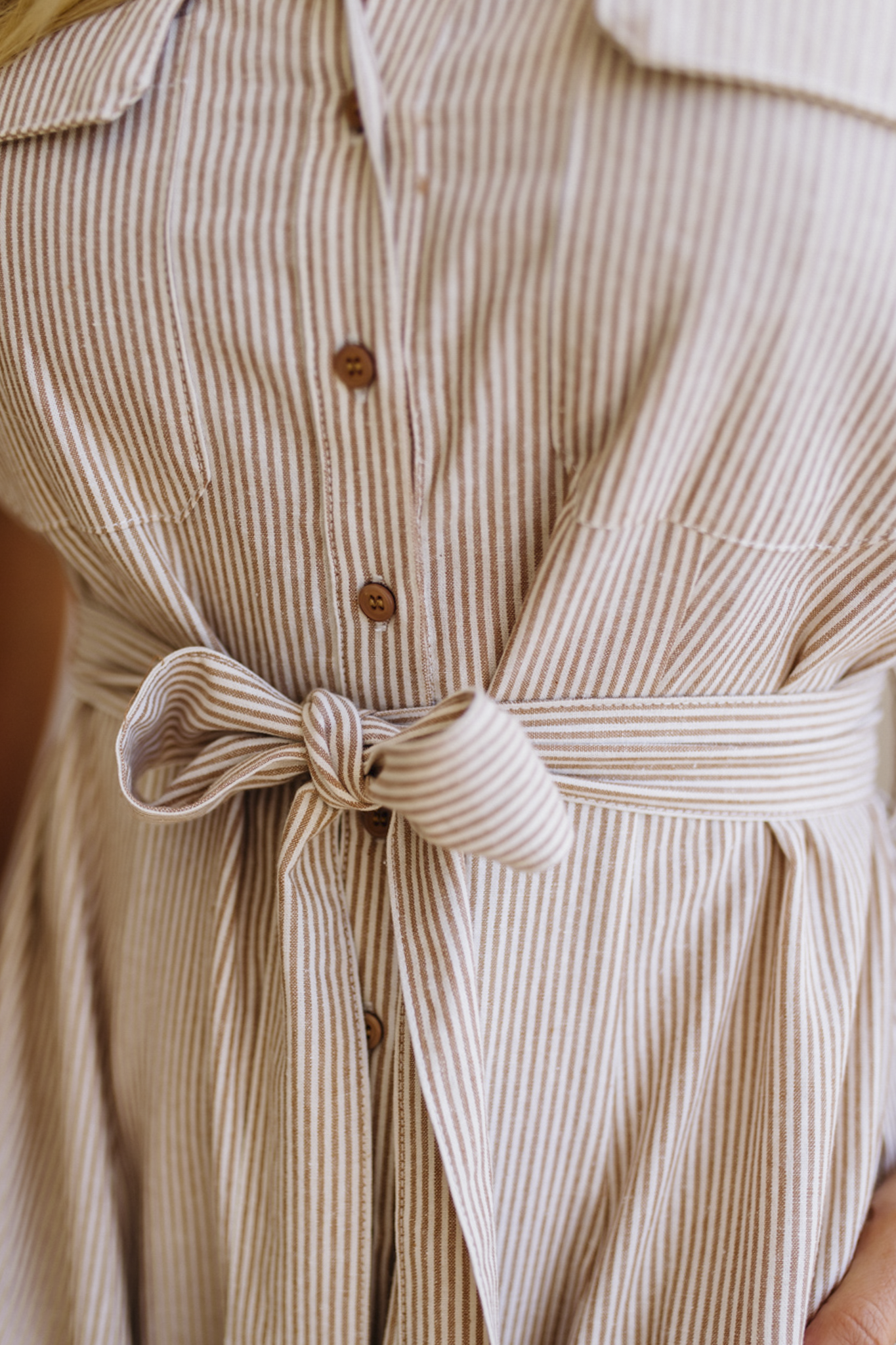 Close-up of a beige and brown striped dress with a tie waist.