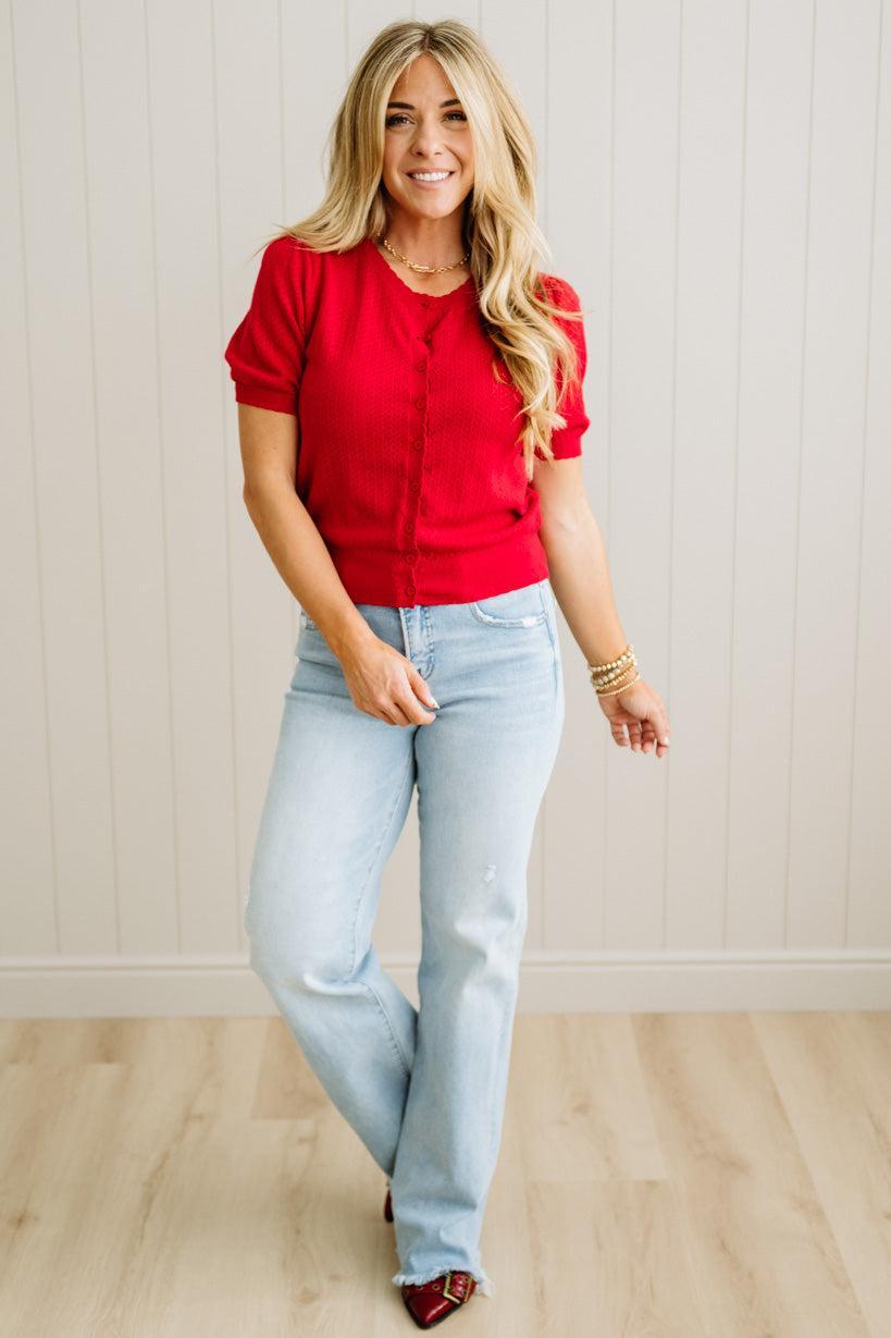 Woman wearing a red top and light blue jeans against a white wall.