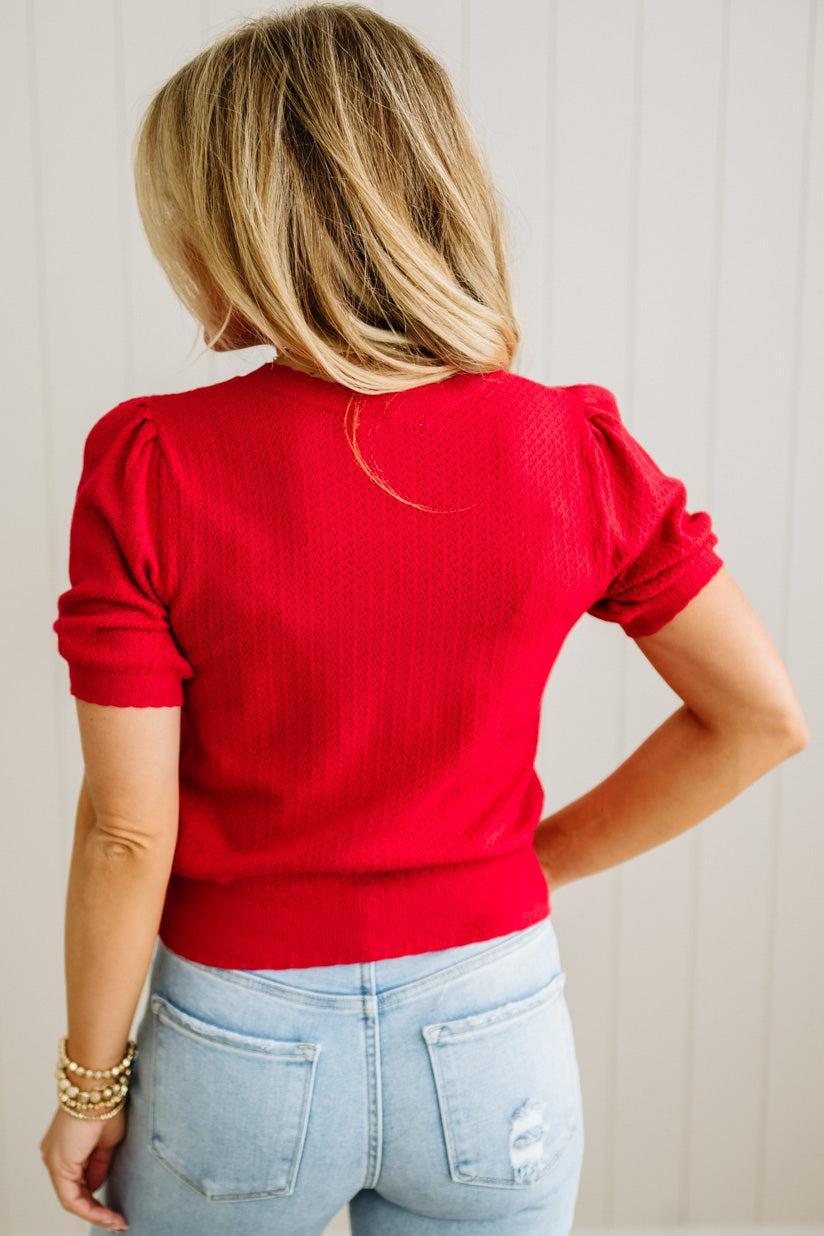 Person wearing a red sweater and light blue jeans with a neutral background