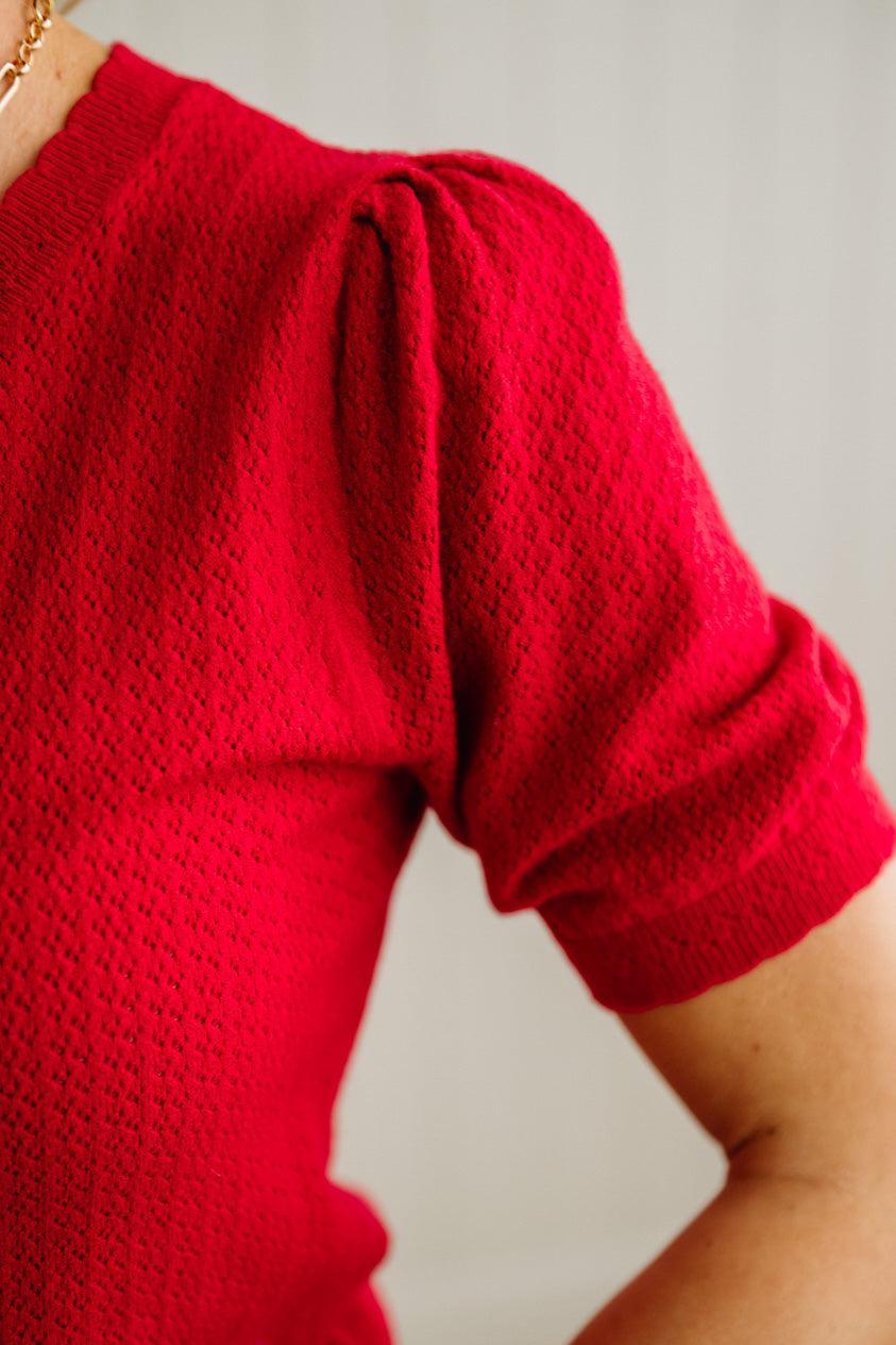 Red knitted top with puff sleeves on a neutral background