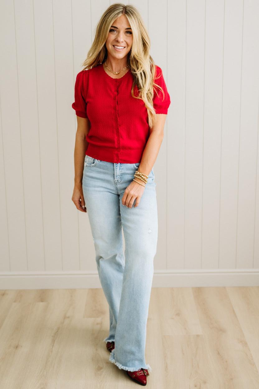 Woman wearing a red top and light blue jeans against a white wall.