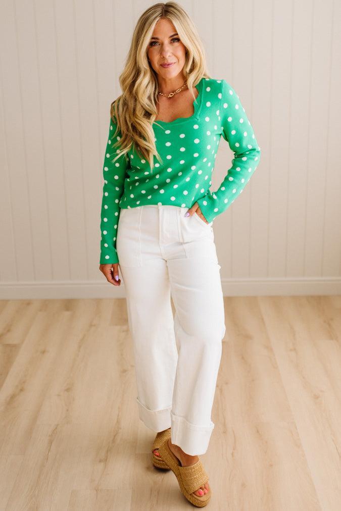 Blonde woman wearing a long sleeve sweater with scalloped square neckline in green with white dots.