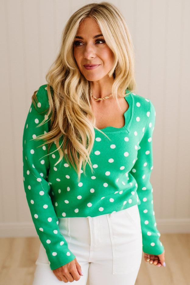 Blonde woman wearing a long sleeve sweater with scalloped square neckline in green with white dots.