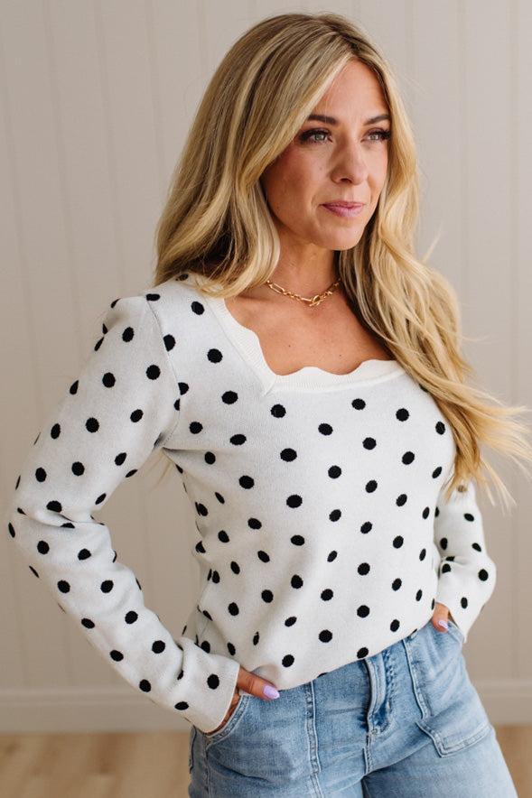 Blonde woman wearing a long sleeve sweater with scalloped square neckline in white with black dots.