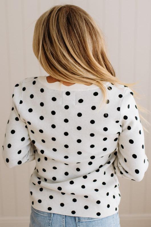 Blonde woman wearing a long sleeve sweater with scalloped square neckline in white with black dots.