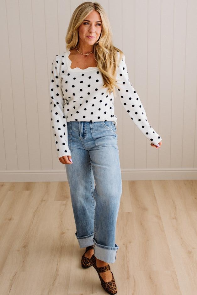 Blonde woman wearing a long sleeve sweater with scalloped square neckline in white with black dots.