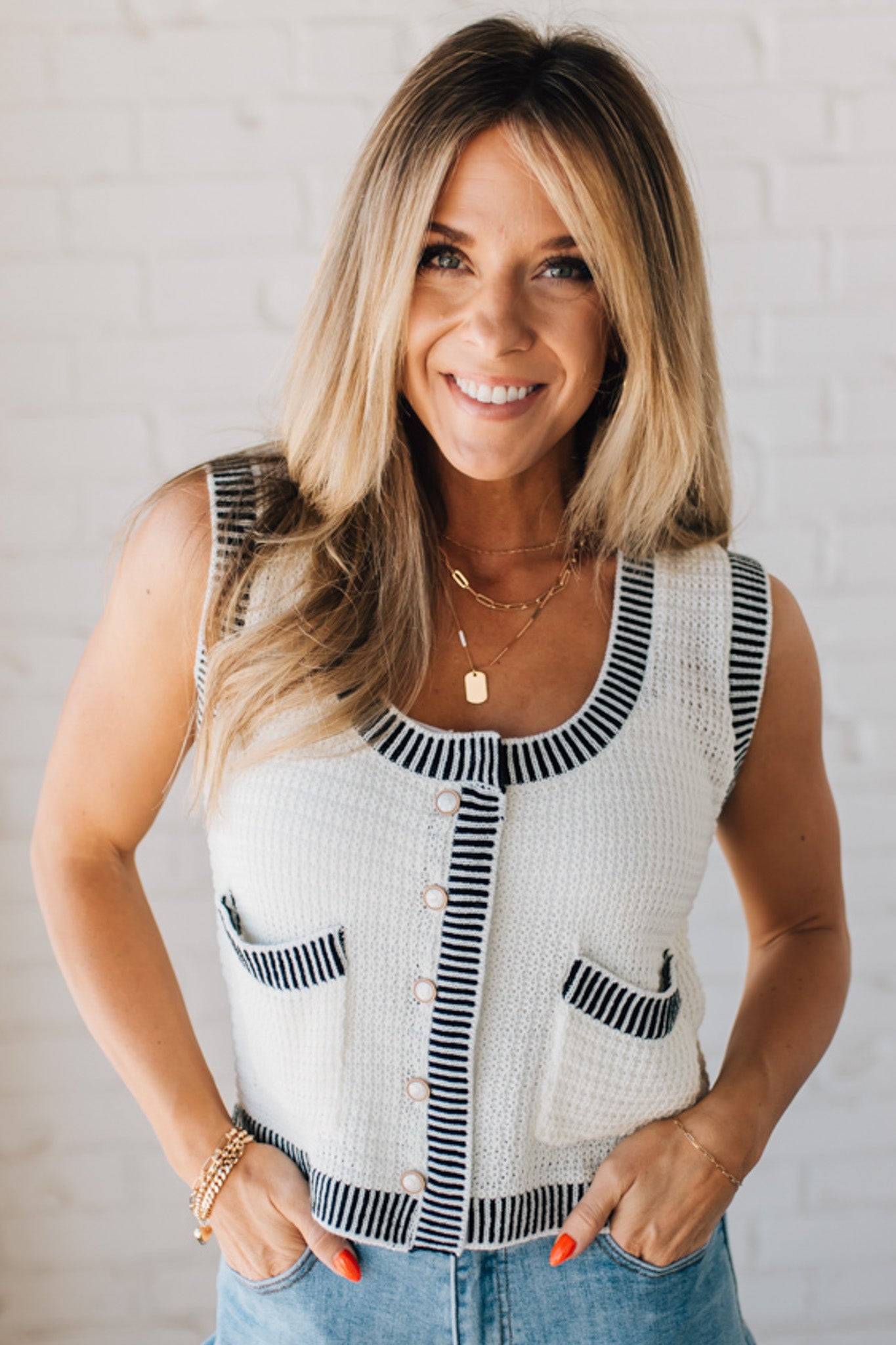 BLONDE WOMAN WEARING A BLACK AND WHITE CONTRAST RIB DETAIL TEXTURED SWEATER VEST WITH PEARL ACCENT BUTTON FRONT.