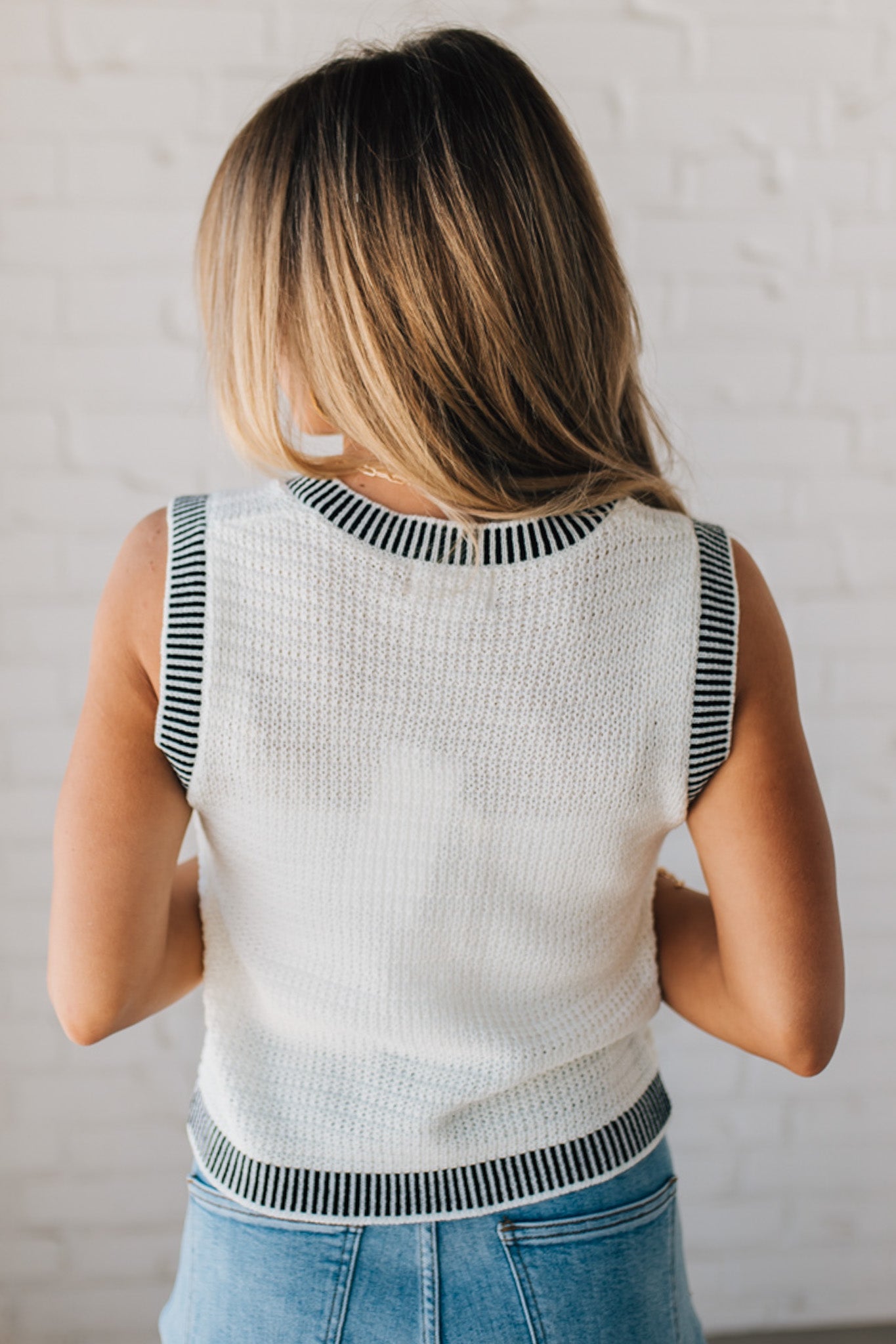 BLONDE WOMAN WEARING A BLACK AND WHITE CONTRAST RIB DETAIL TEXTURED SWEATER VEST WITH PEARL ACCENT BUTTON FRONT.