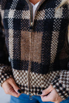 Person wearing a checkered zip-up sweater with a blurred background