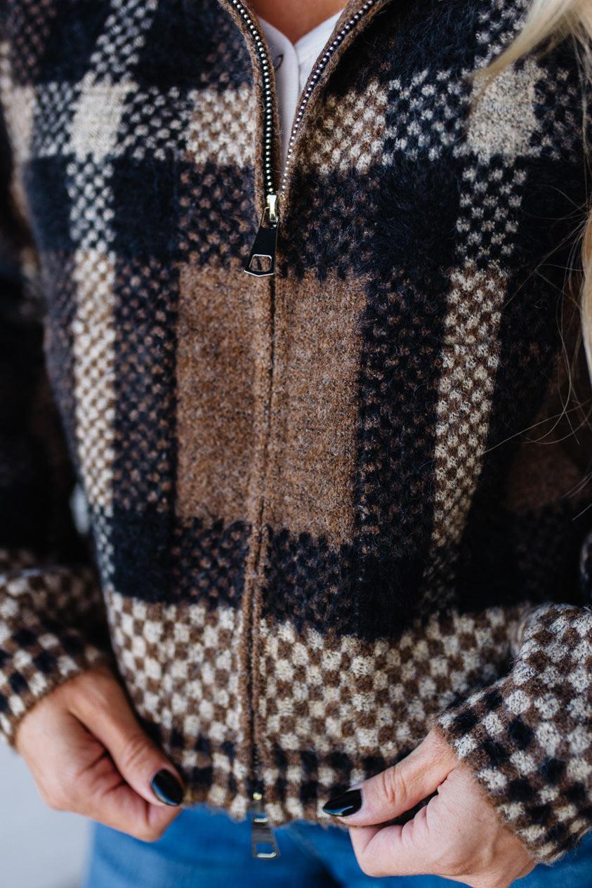Person wearing a checkered zip-up sweater with a blurred background