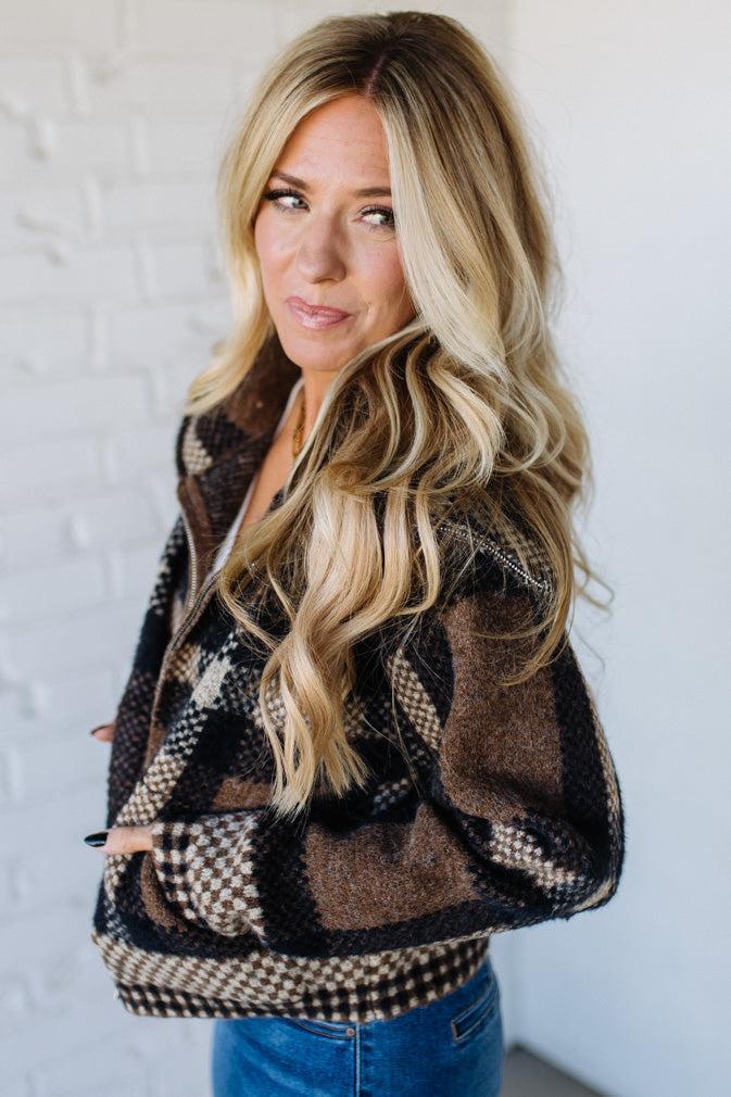 Woman wearing a patterned jacket against a white brick wall