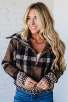 Woman wearing a plaid jacket against a white brick wall