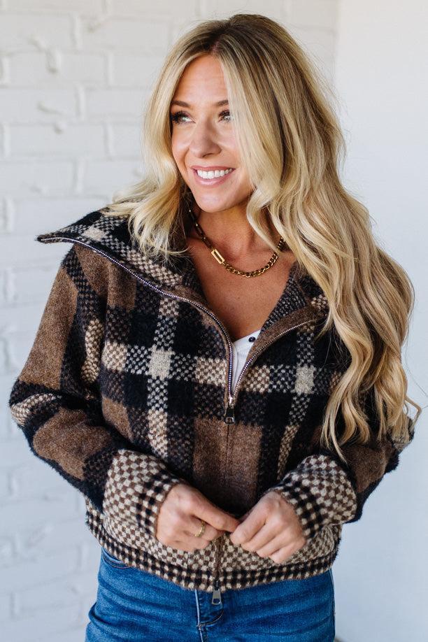 Woman wearing a plaid jacket against a white brick wall