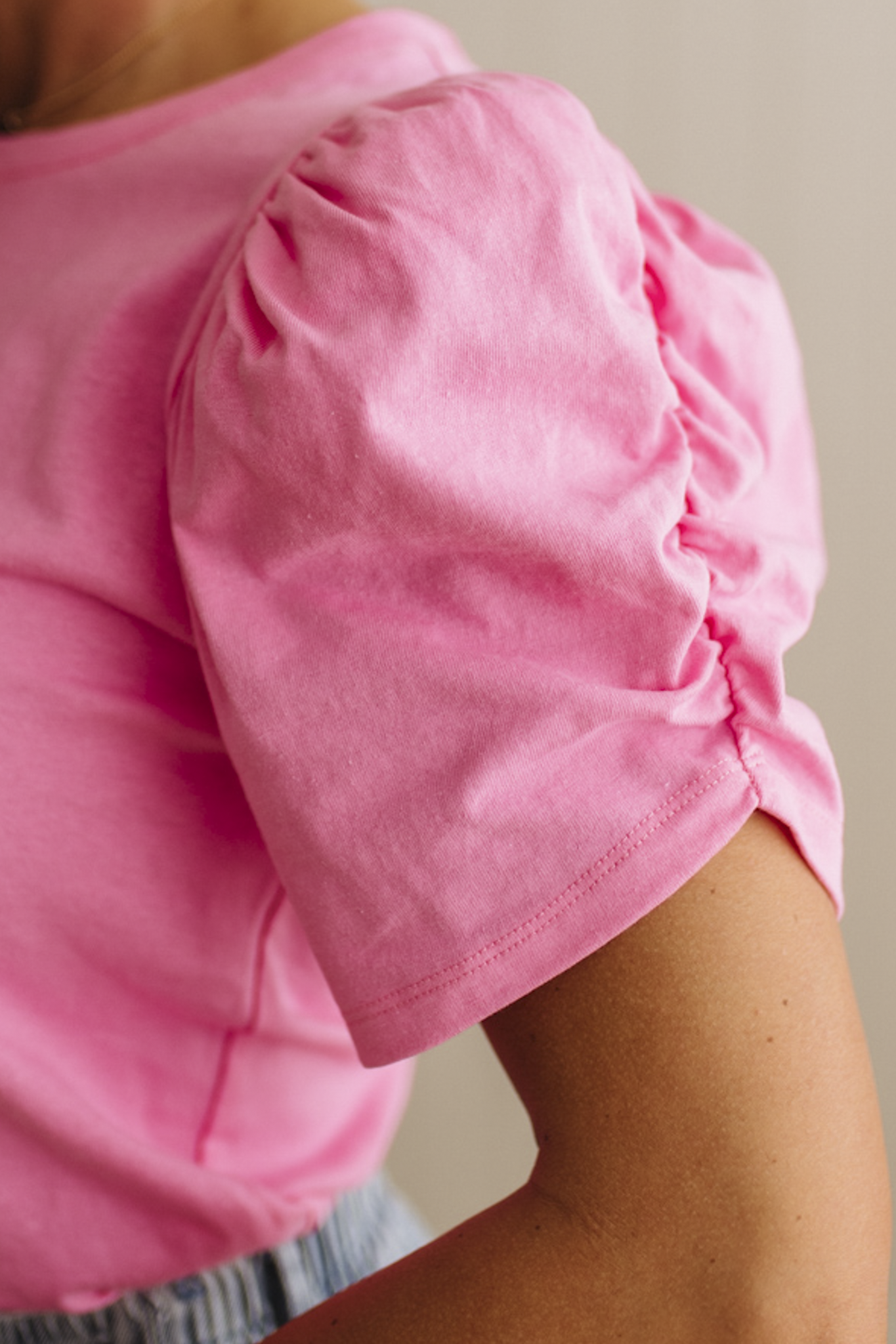 Woman wearing a pink top standing against a beige wall.