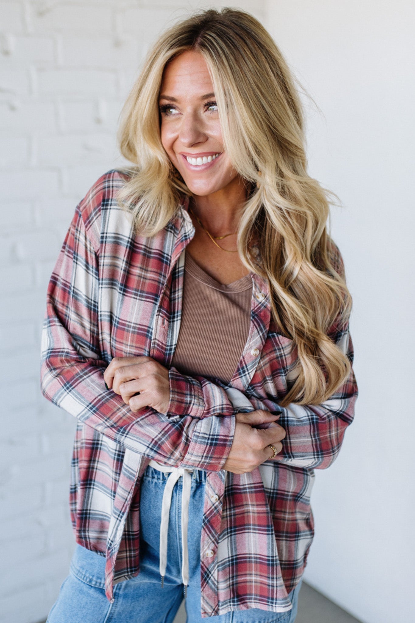 Woman wearing a plaid shirt over a brown top and jeans against a white background