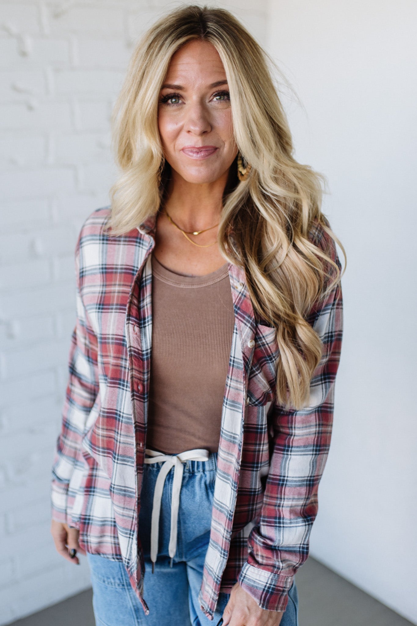 Woman wearing a plaid shirt over a brown top and blue jeans against a white background