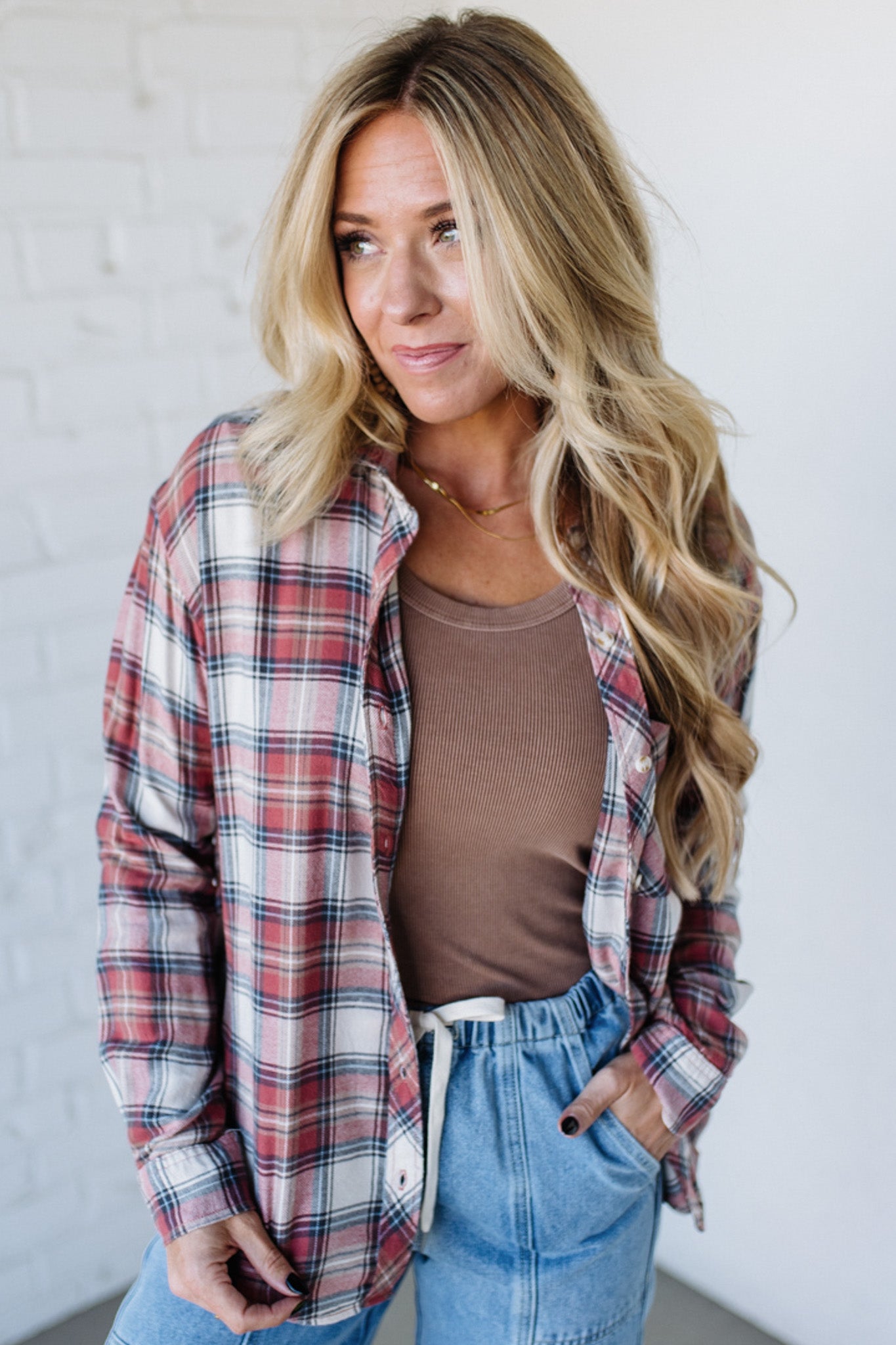 Woman wearing a plaid shirt, brown top, and blue jeans against a white background