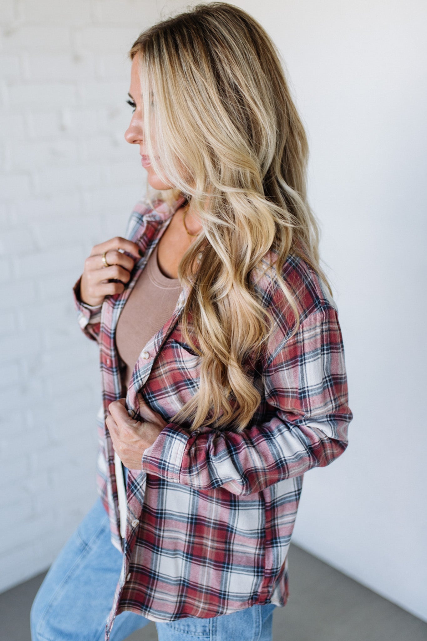 Woman wearing a plaid shirt and jeans against a white wall