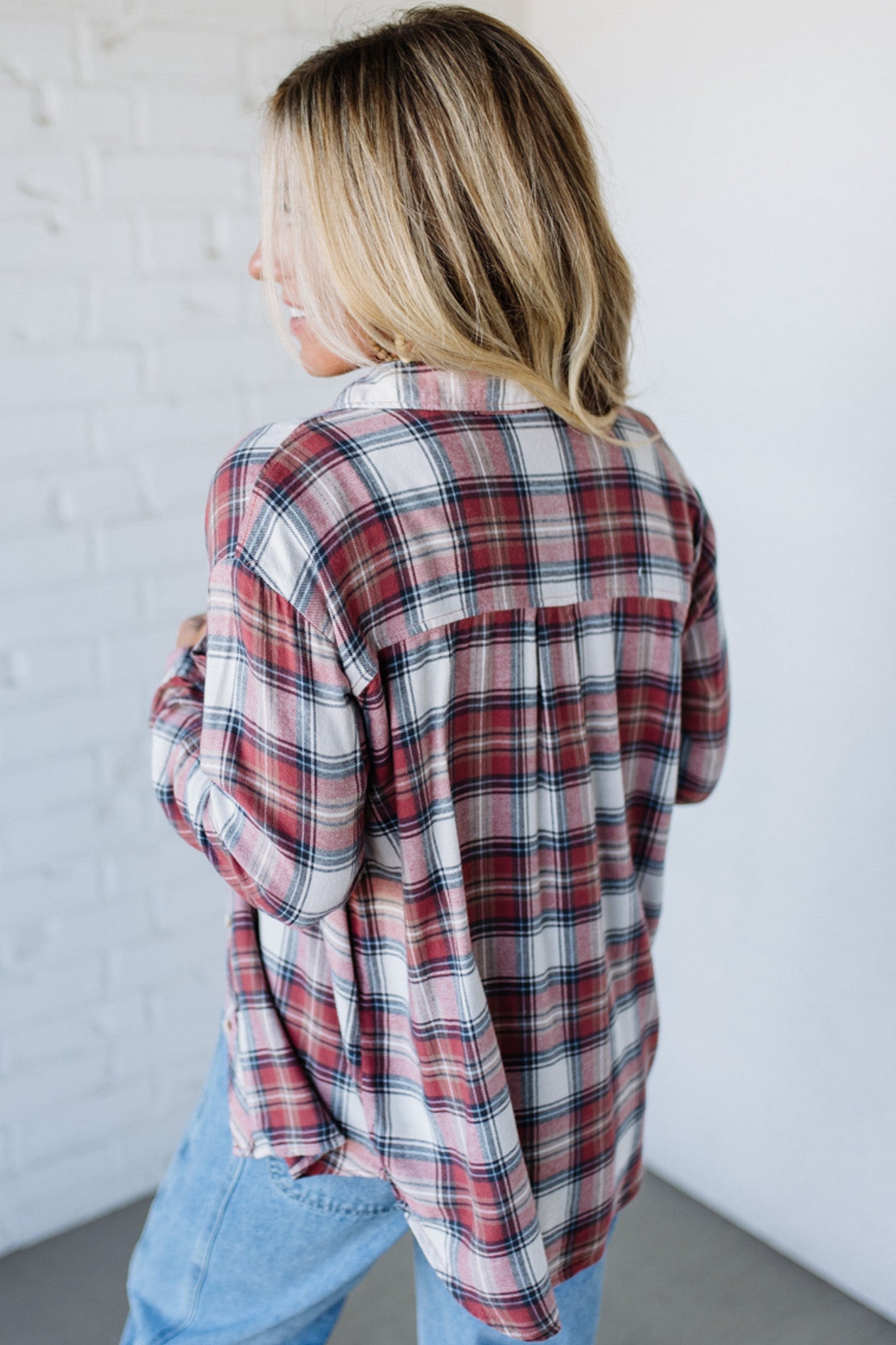 Person wearing a plaid shirt and jeans against a white wall