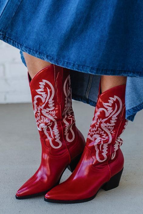 Red cowboy boots with white embroidery worn with a blue denim skirt.