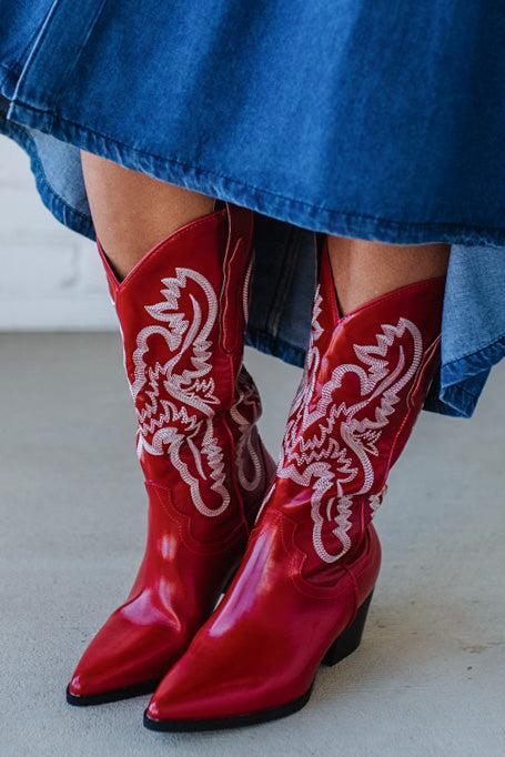 Red cowboy boots with white patterns worn with a blue denim skirt.