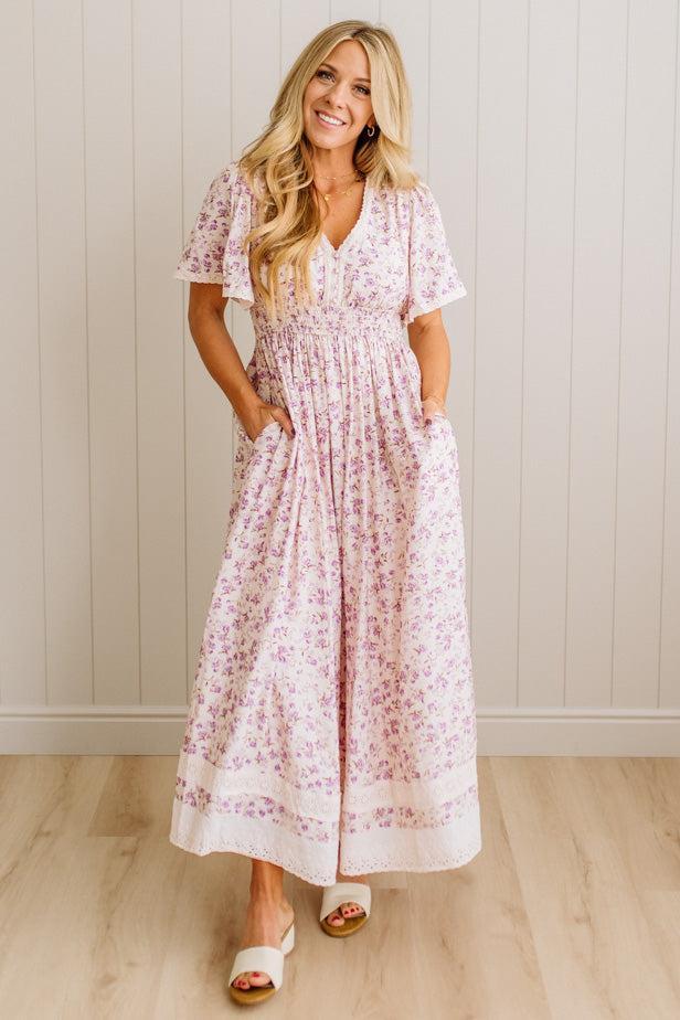 Woman wearing a floral dress standing against a white paneled wall.