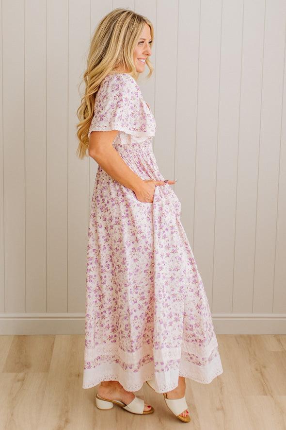 Woman wearing a floral dress standing against a plain wall.