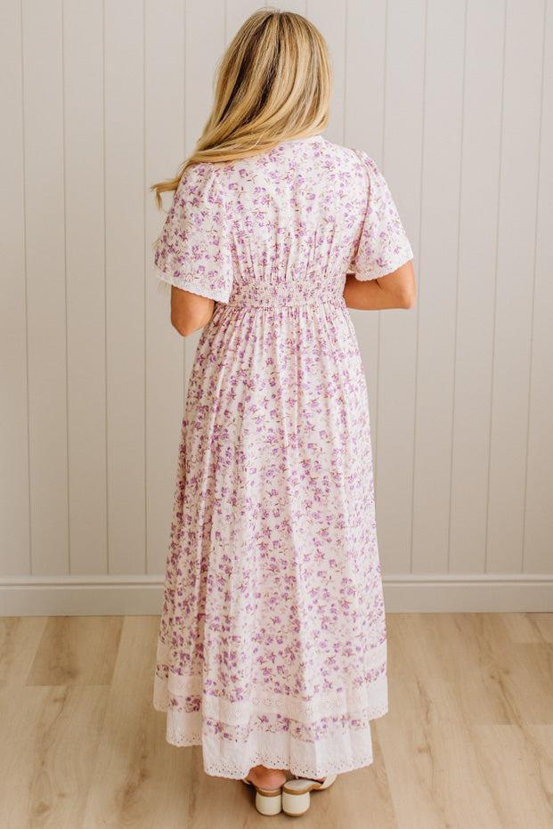 Woman wearing a floral dress standing against a plain wall.