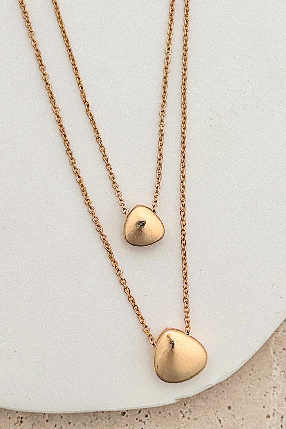 Two gold heart-shaped pendants on delicate chains against a light background