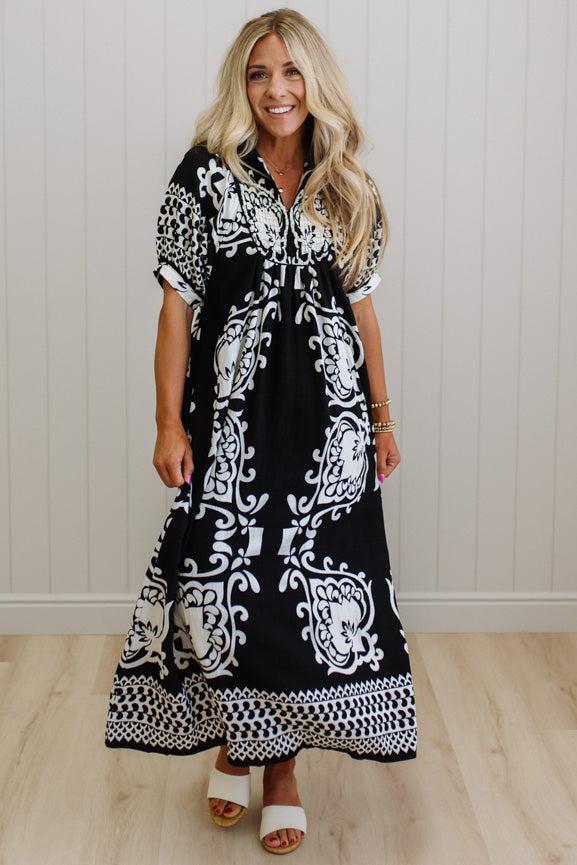 Woman wearing a black and white patterned dress against a white wall.