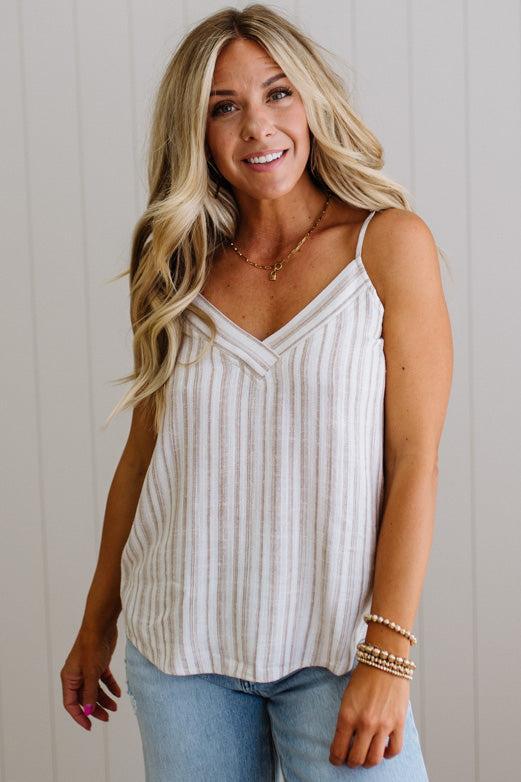 Woman wearing a striped tank top and jeans against a light wooden panel background