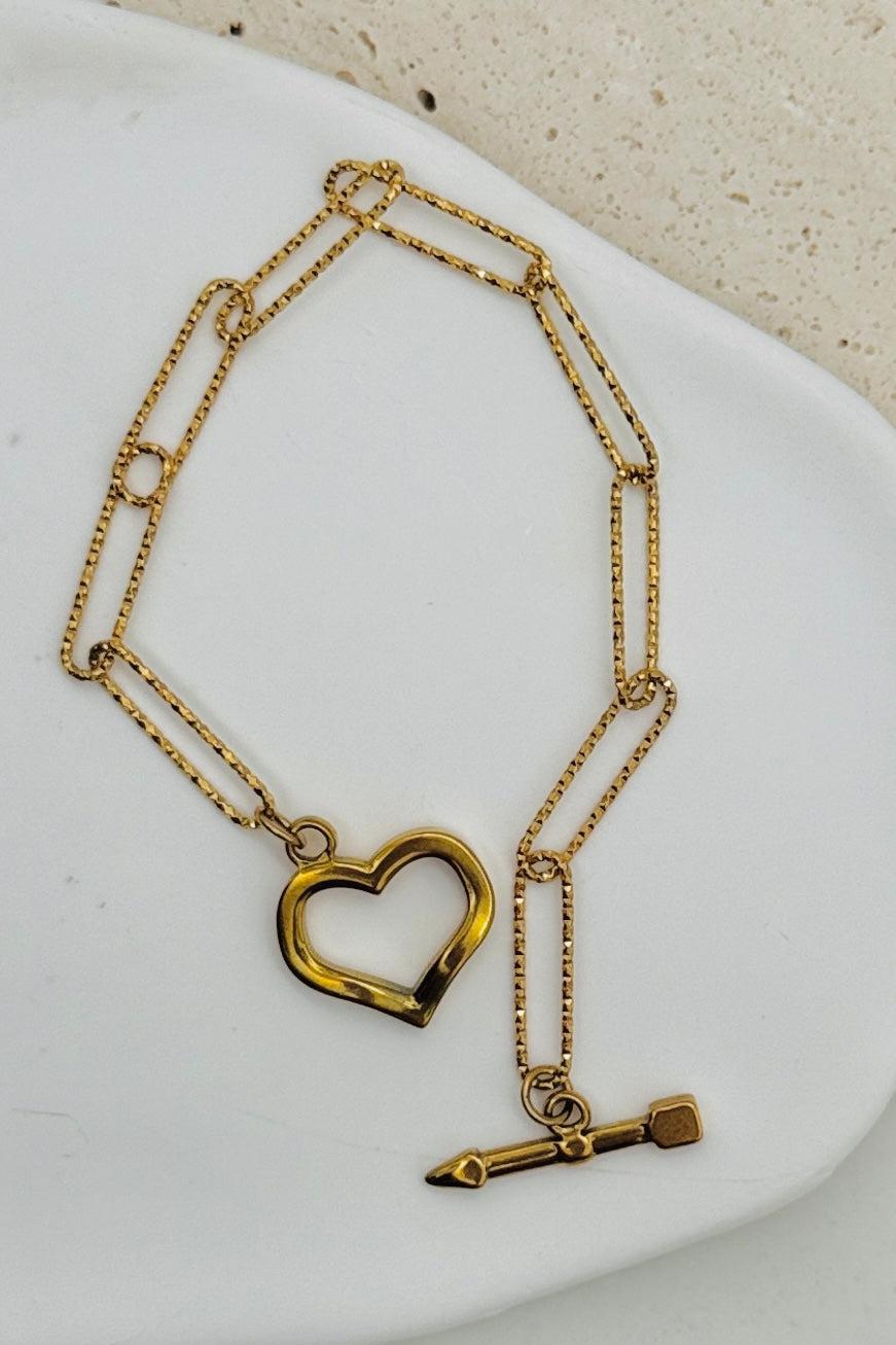 Gold necklace with heart and arrow pendant on a white dish