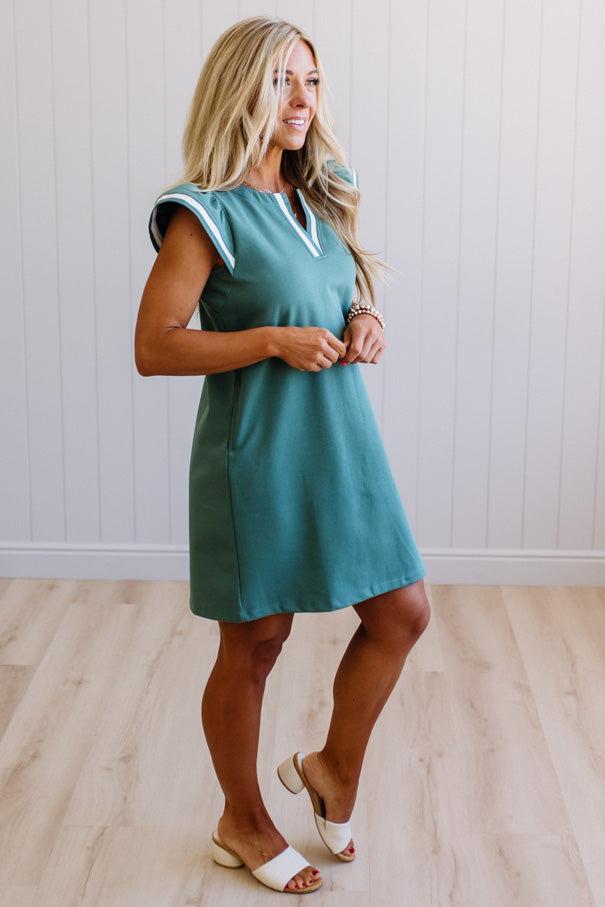Woman wearing a teal dress with white trim in a minimalistic setting