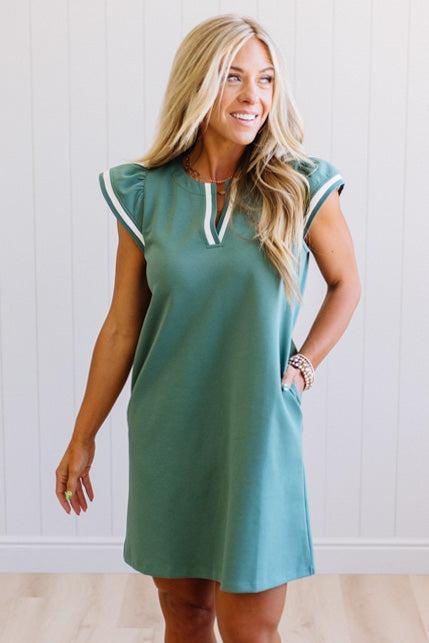 Woman wearing a green dress with white trim against a white background